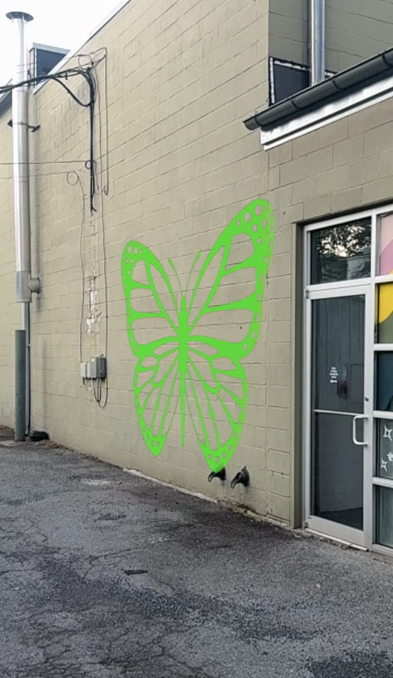 Phone screenshot of the butterfly drawing cast onto a real building wall in mural mode